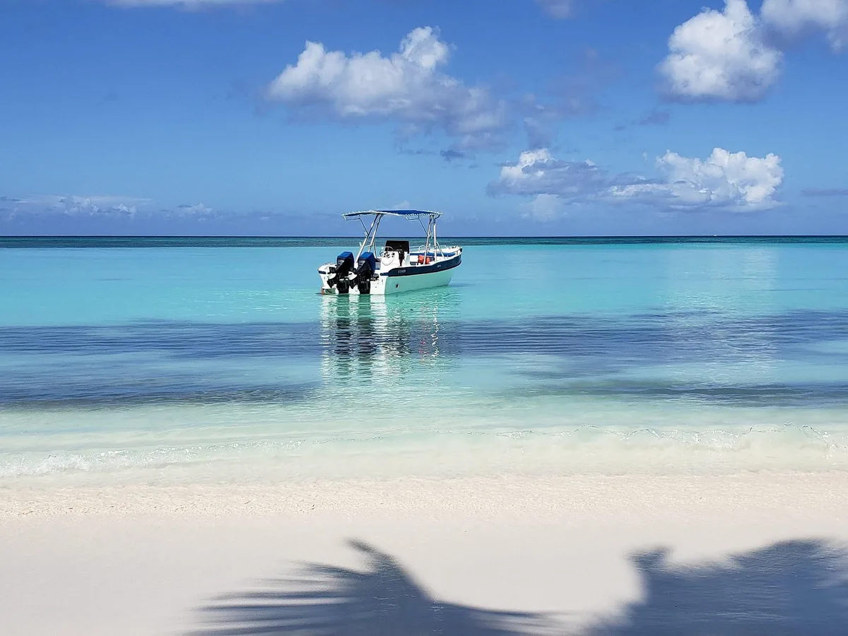 A small white speedboat anchored in turquoise shallows off a white beach