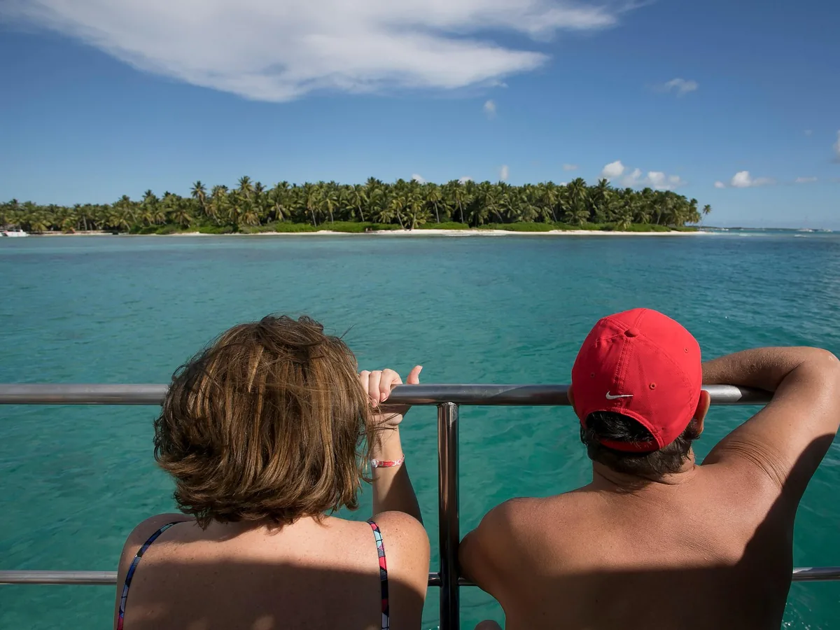 Zwei Reisende von hinten an der Reling, Blick auf eine palmenbewachsene Insel